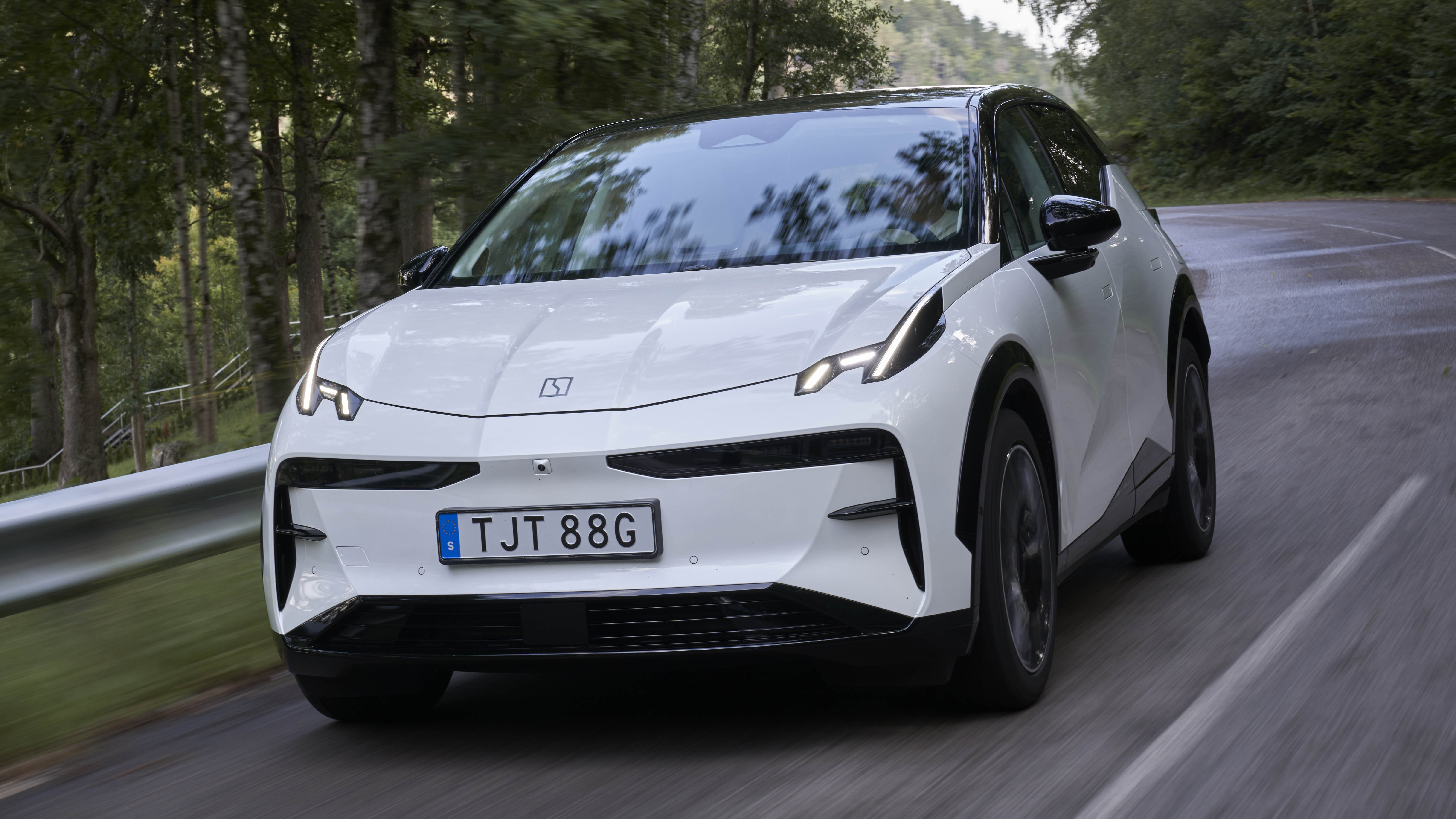 Un SUV compact électrique Zeekr X de couleur vive roule sur une route sinueuse avec un paysage montagneux en arrière-plan.