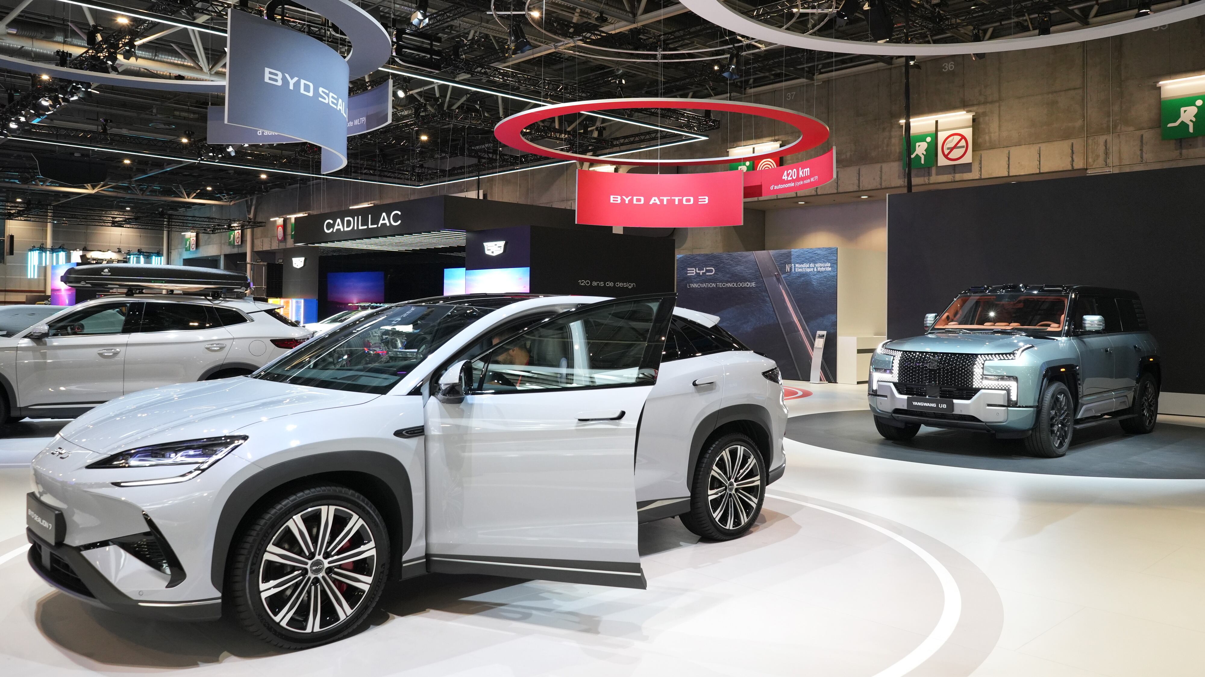 L'intérieur d'un showroom BYD moderne et lumineux, présentant plusieurs modèles de voitures électriques BYD. Des clients et des vendeurs discutent autour des véhicules.