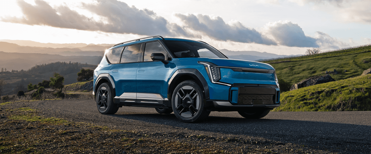 Vue extérieure d'un Kia EV9 de couleur vive, garé sur une route de montagne, mettant en valeur son design moderne et sa taille imposante.