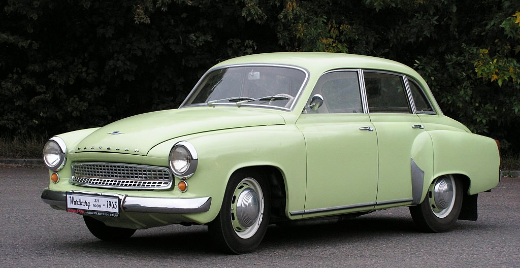 Photographie d'une Wartburg 311 d'époque, de couleur claire, garée dans une rue pavée.