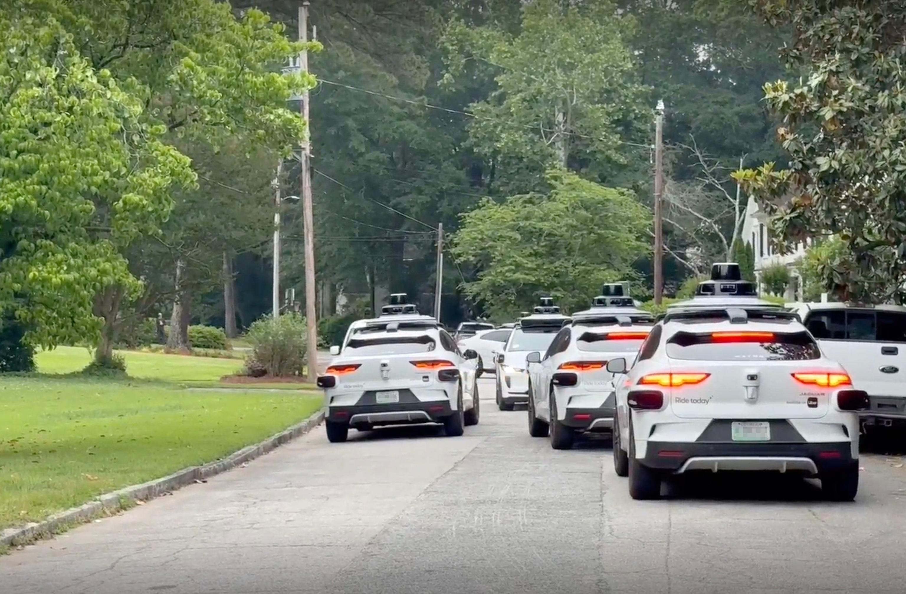 Plusieurs voitures autonomes Waymo jaunes et blanches sont immobilisées dans une rue résidentielle étroite, certaines tentant de faire demi-tour, d'autres à l'arrêt, sous un ciel bleu clair.