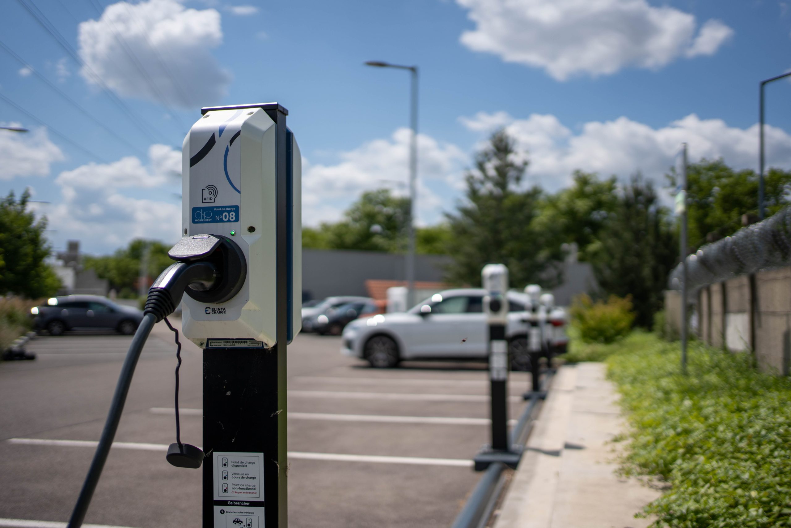 Une personne utilisant son smartphone pour recharger facilement son véhicule électrique à une borne de recharge rapide en milieu urbain en France.