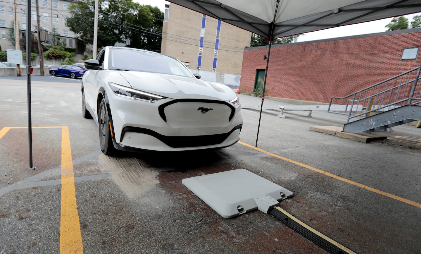 Image d'une voiture électrique garée au-dessus d'une plaque de recharge sans fil au sol, sans aucun câble visible.