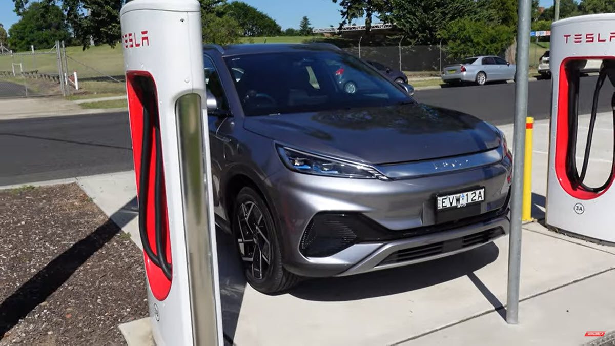 Une voiture électrique BYD Atto 3 grise en train de charger à une borne de recharge en ville.