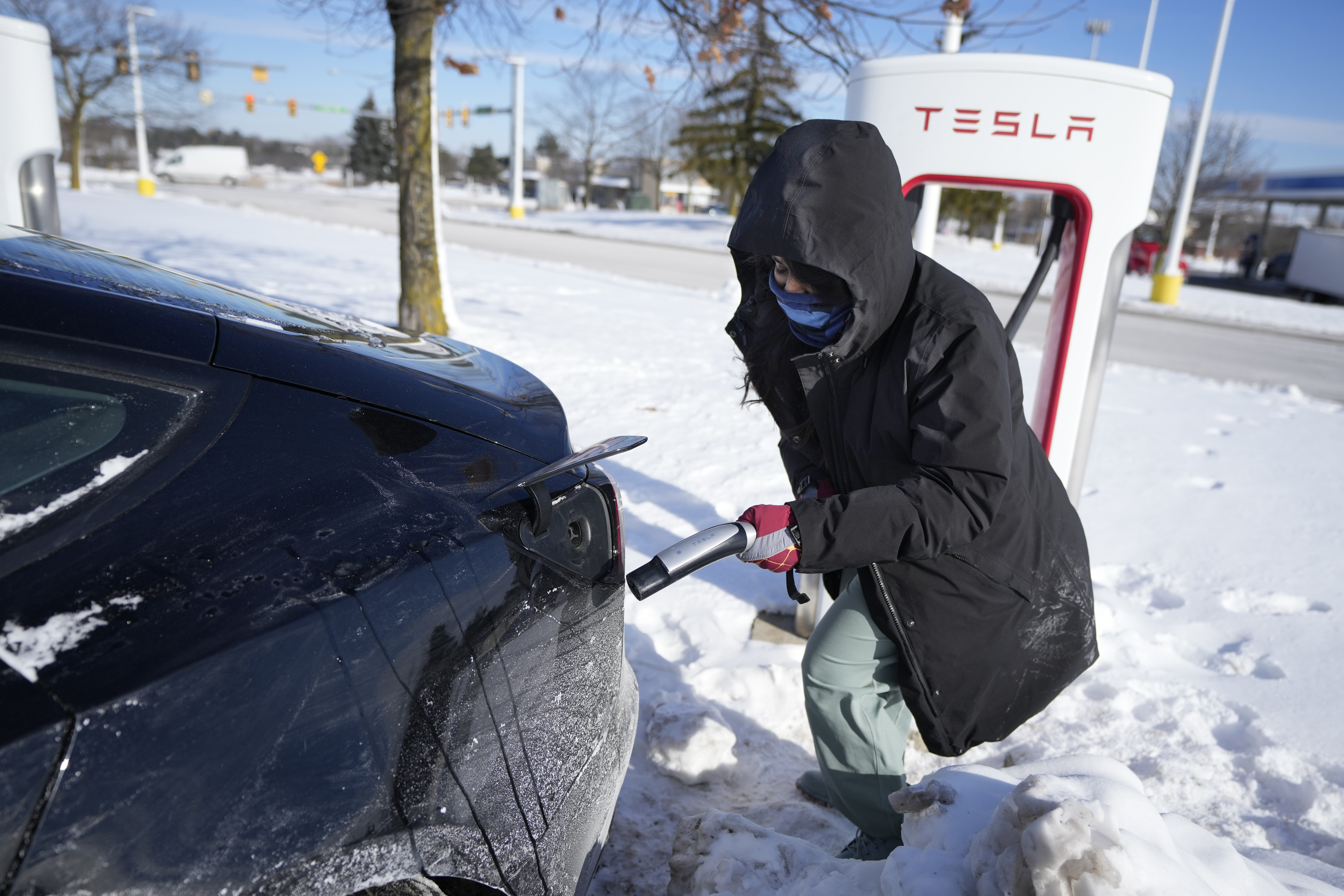 Une voiture électrique blanche branchée à une borne de recharge dans un garage, avec un léger givre sur la carrosserie.