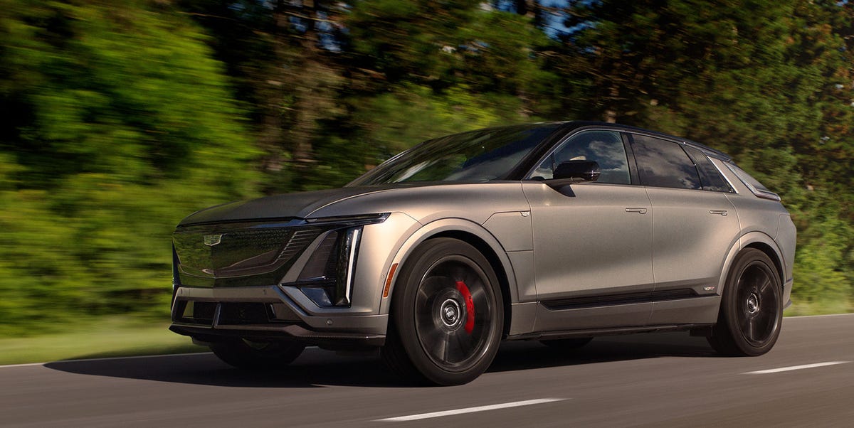 Un SUV électrique Cadillac Lyriq argenté roulant sur une route côtière au coucher du soleil, avec l'océan en arrière-plan.