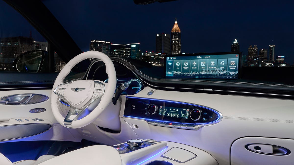 Intérieur luxueux d'un Genesis Electrified GV70, montrant le tableau de bord avec un grand écran, des sièges en cuir clair et des accents en bois.