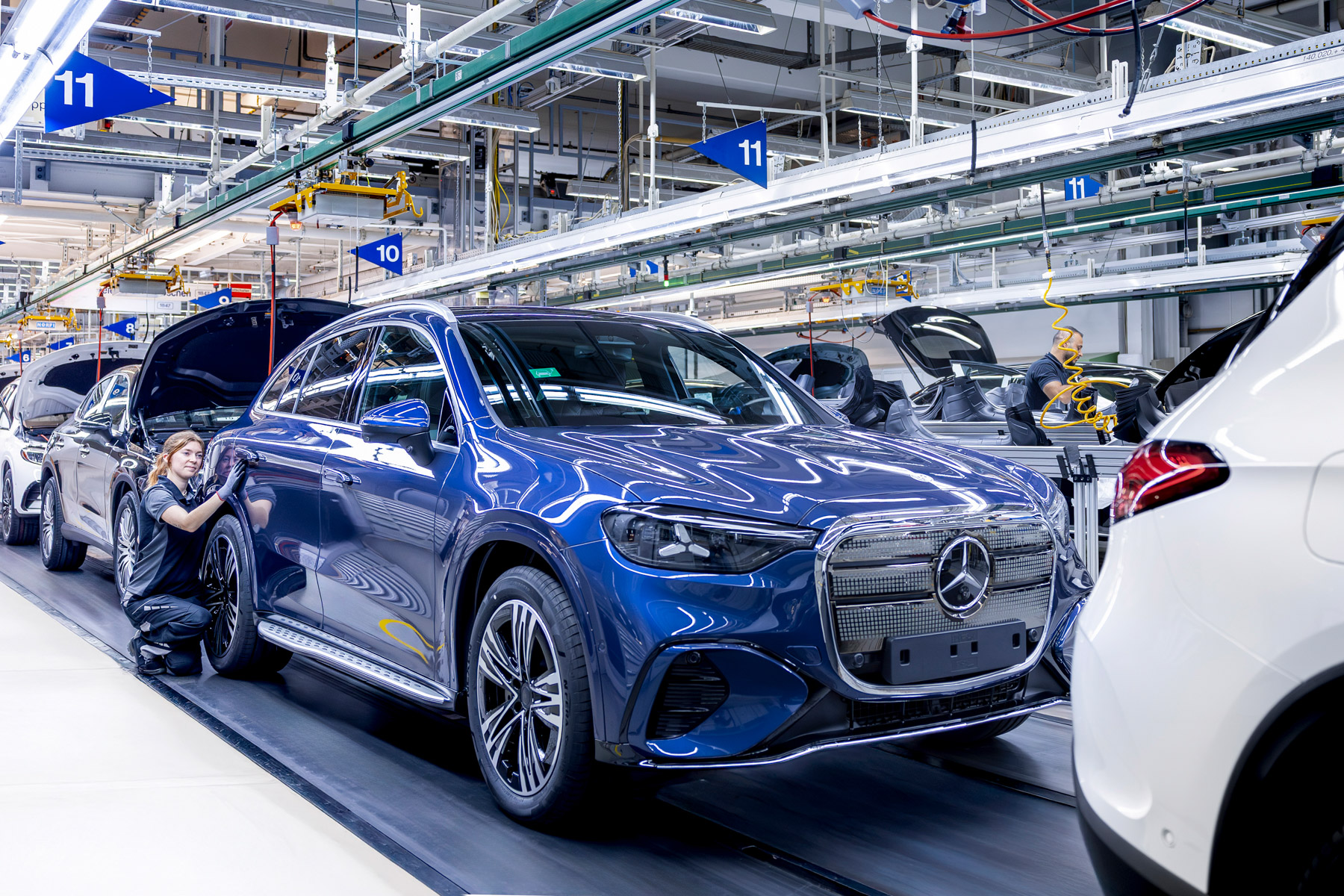 Une image aérienne d'une usine Mercedes-Benz moderne et bien éclairée, montrant la ligne d'assemblage du GLC électrique avec des robots et des ouvriers.