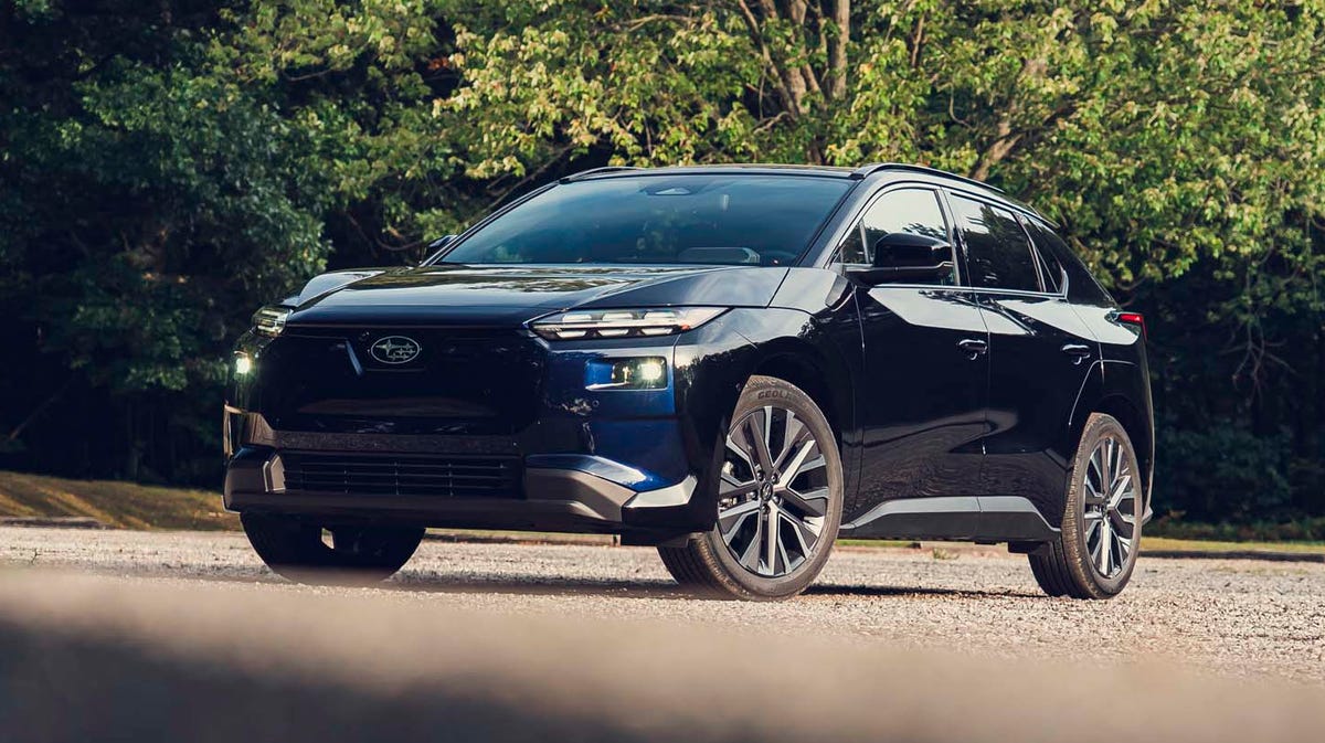 Vue extérieure d'un SUV électrique Subaru de couleur sombre, garé sur une route de montagne sinueuse avec un ciel bleu clair.