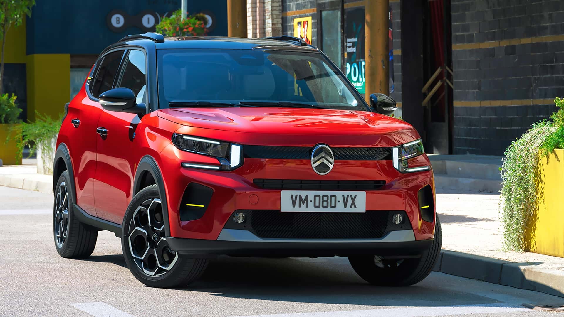 Une Citroën ë-C3 électrique de 2024, de couleur vive, garée dans une rue urbaine avec des bâtiments modernes en arrière-plan.