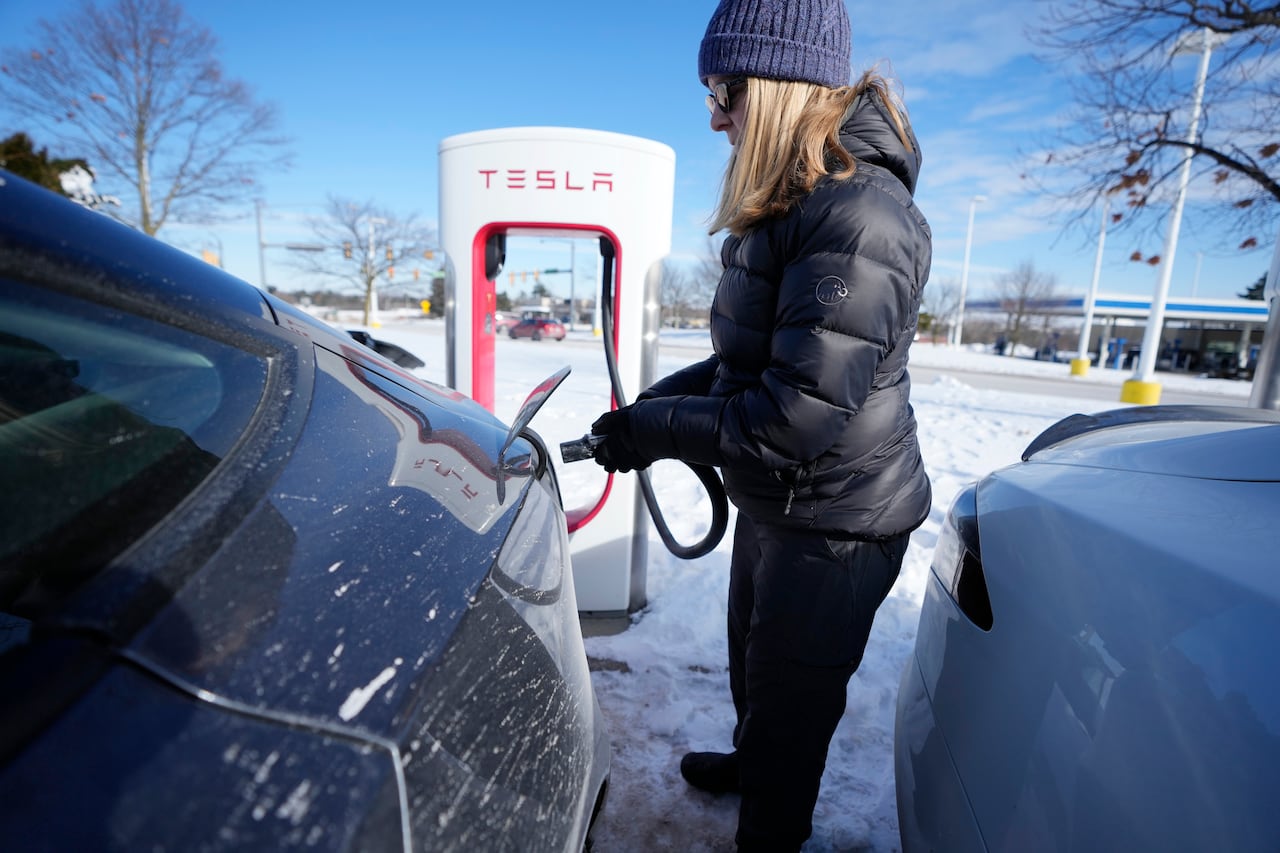 Une voiture électrique blanche branchée à une borne de recharge rapide dans un paysage hivernal enneigé au Canada. La voiture et la borne sont légèrement recouvertes de neige.