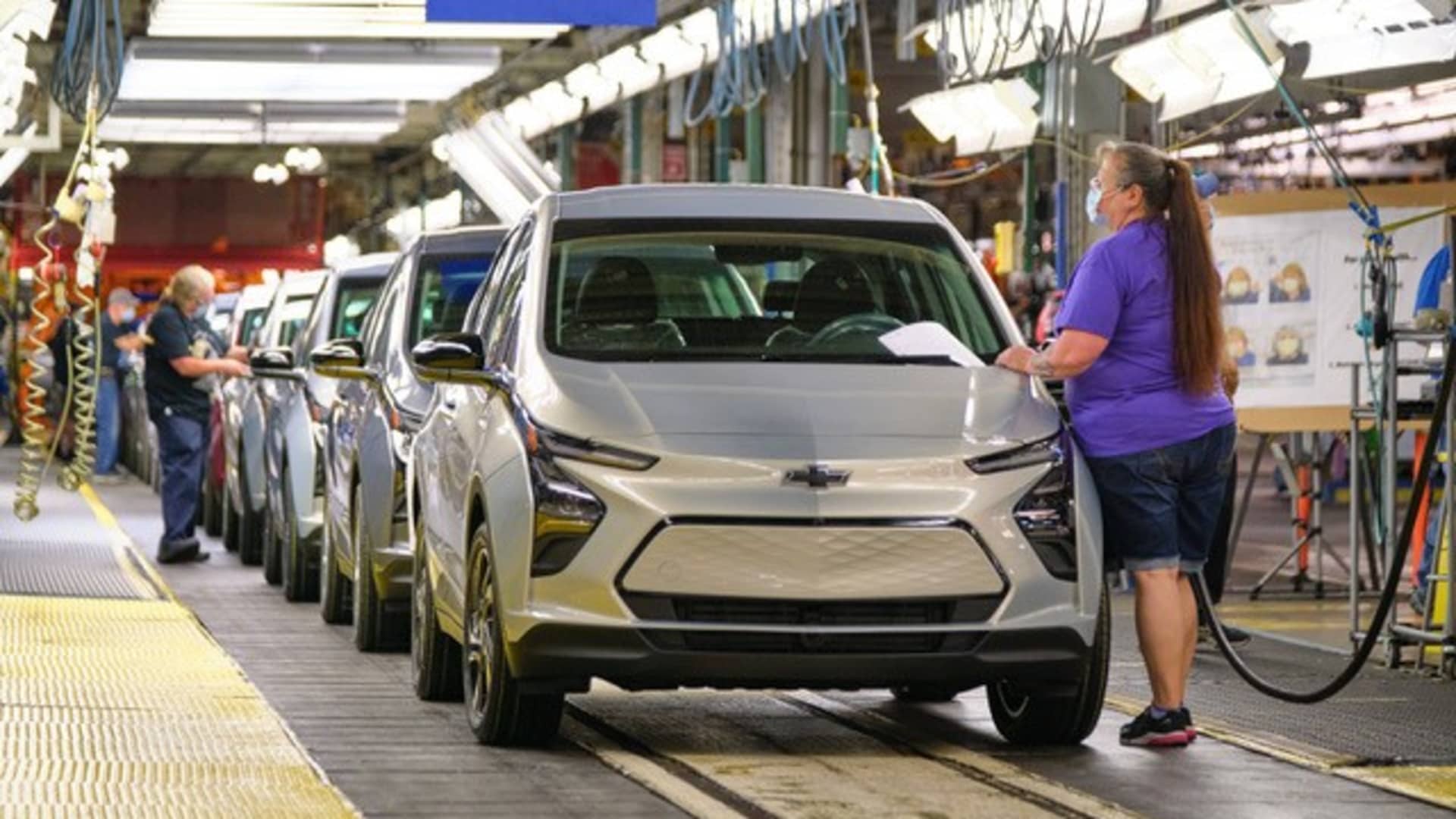 Une Chevrolet Bolt EV en cours d'assemblage sur une chaîne de production, avec des ouvriers en arrière-plan.