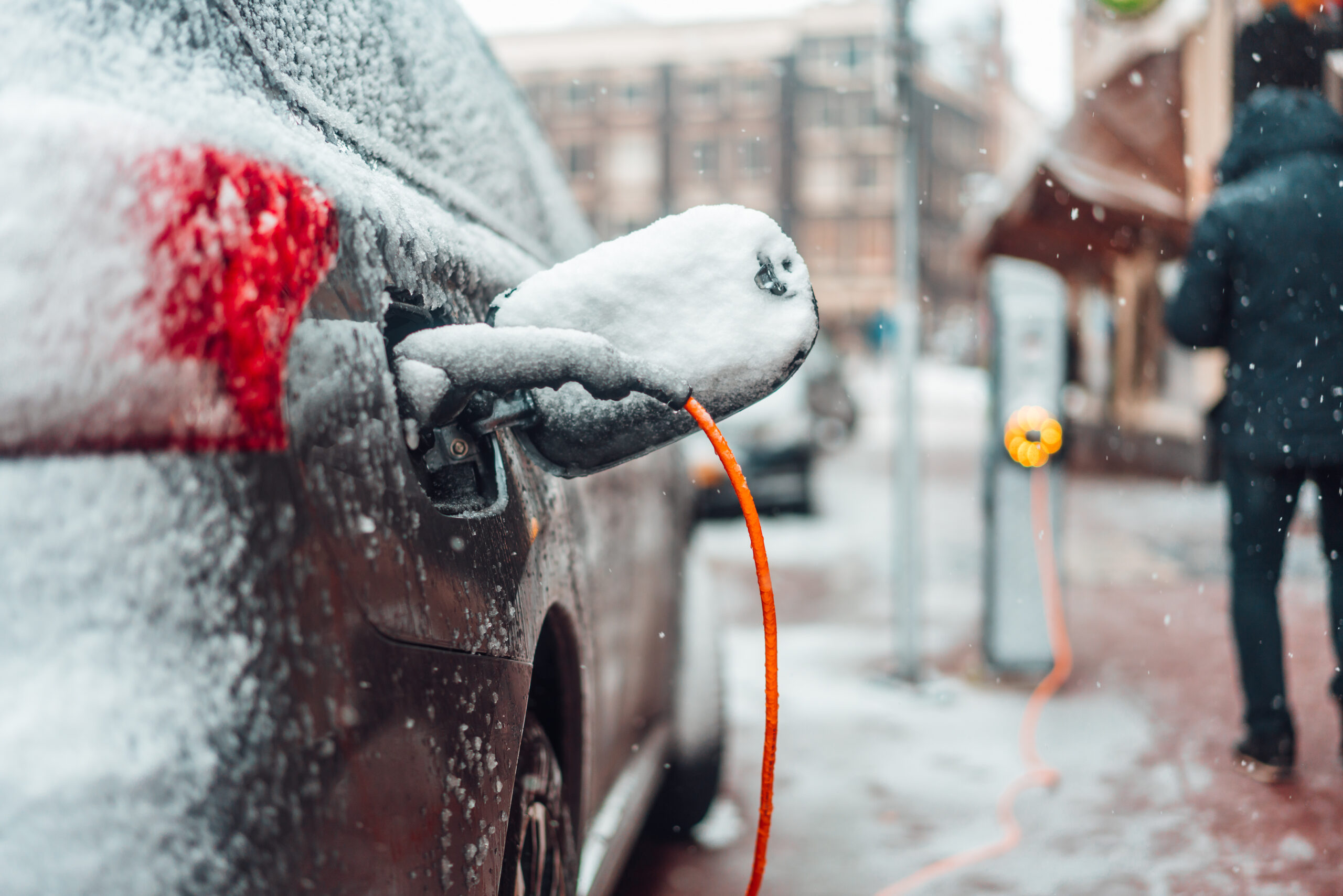 Une voiture électrique blanche en charge sur une borne publique, entourée de neige et de glace, avec un paysage hivernal en arrière-plan.