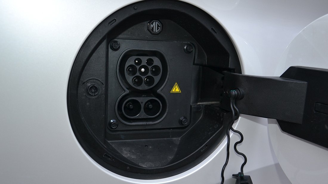 Un SUV électrique MG Marvel R blanc est en train de charger, avec le câble connecté au port de charge visible sur le côté du véhicule.