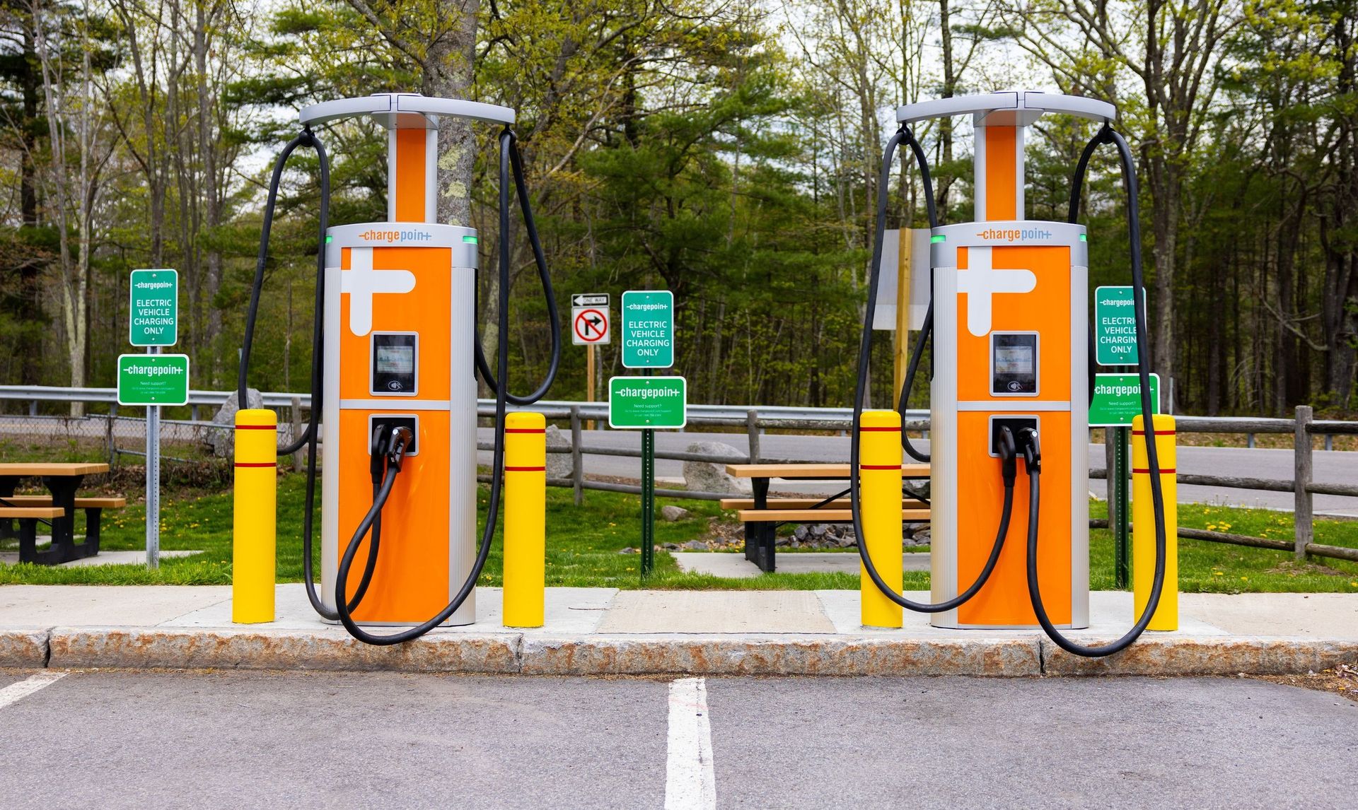 Une station de recharge moderne et bien éclairée sur une autoroute, avec plusieurs bornes de recharge et des voitures électriques en train de recharger.