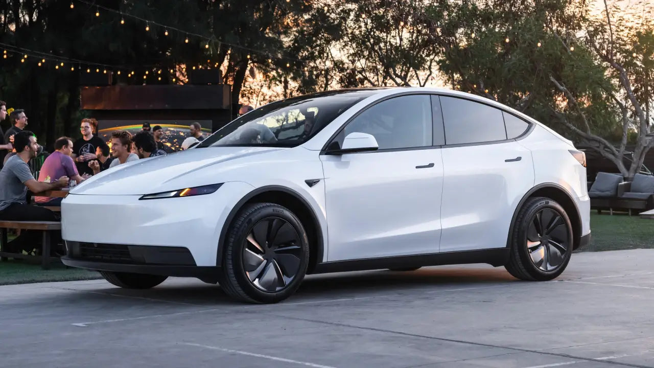 Une Tesla Model Y 2026 blanche roule sur une route de campagne en France, avec des bâtiments traditionnels français en arrière-plan.