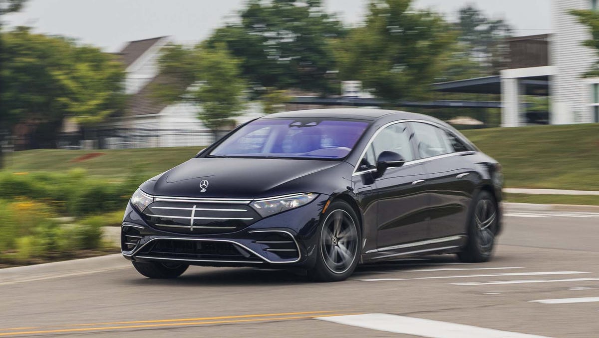Une Mercedes-Benz EQS Limousine 2026 argentée, garée devant un bâtiment moderne, reflétant le soleil couchant.