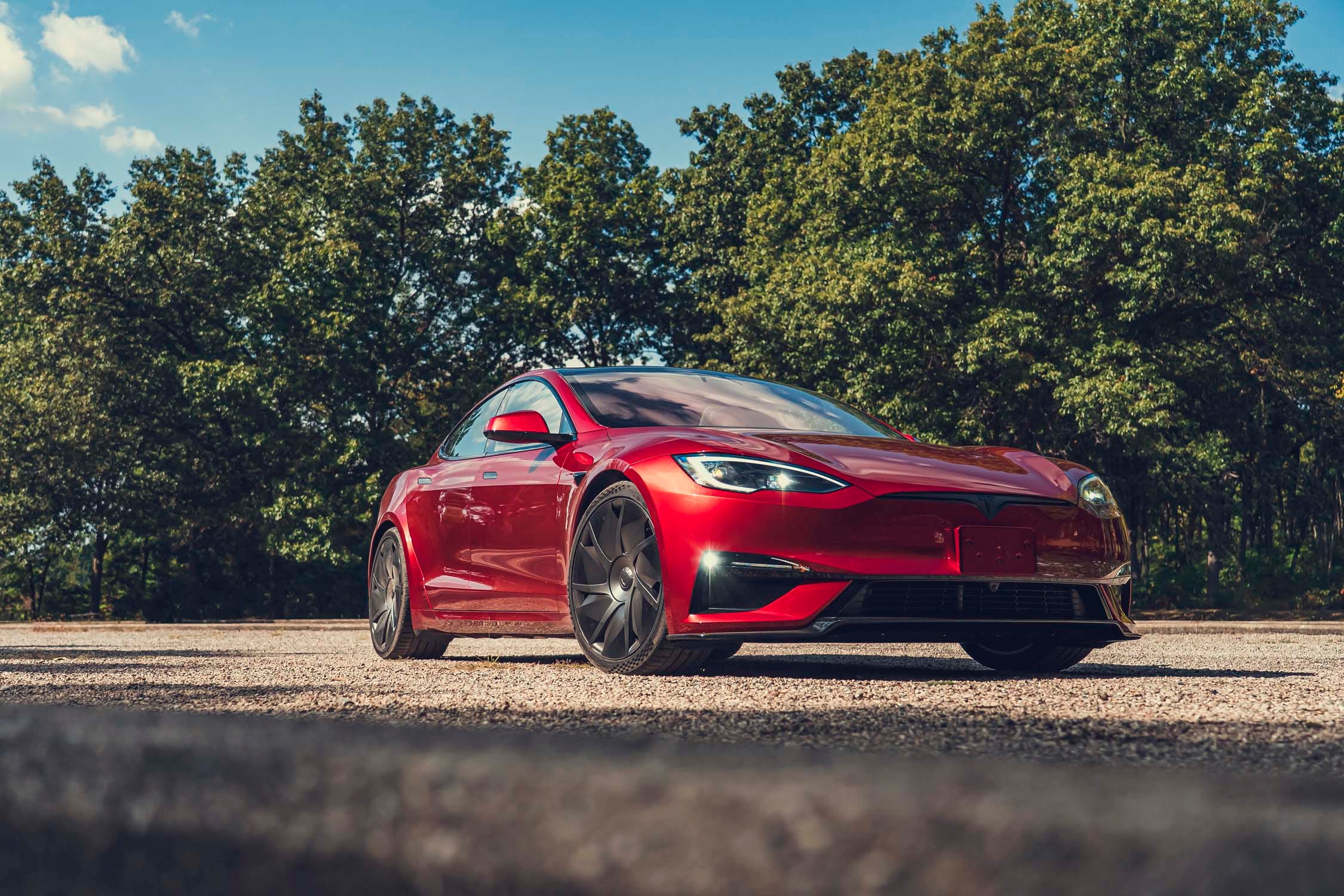 Une Tesla Model S Plaid 2026 rouge vif, roulant sur une route côtière au coucher du soleil.