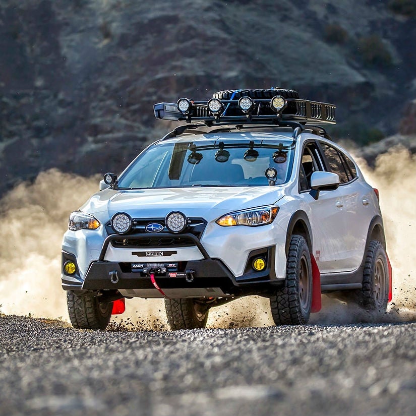 Un SUV Subaru bleu foncé roulant sur un chemin de terre rocailleux avec des montagnes en arrière-plan.