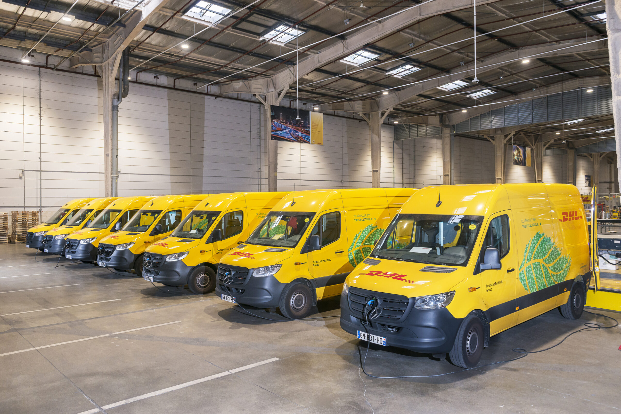 Un fourgon de livraison électrique DHL Express est en charge dans un dépôt en France, illustrant l'investissement des grandes entreprises dans l'électrification de leurs flottes.
