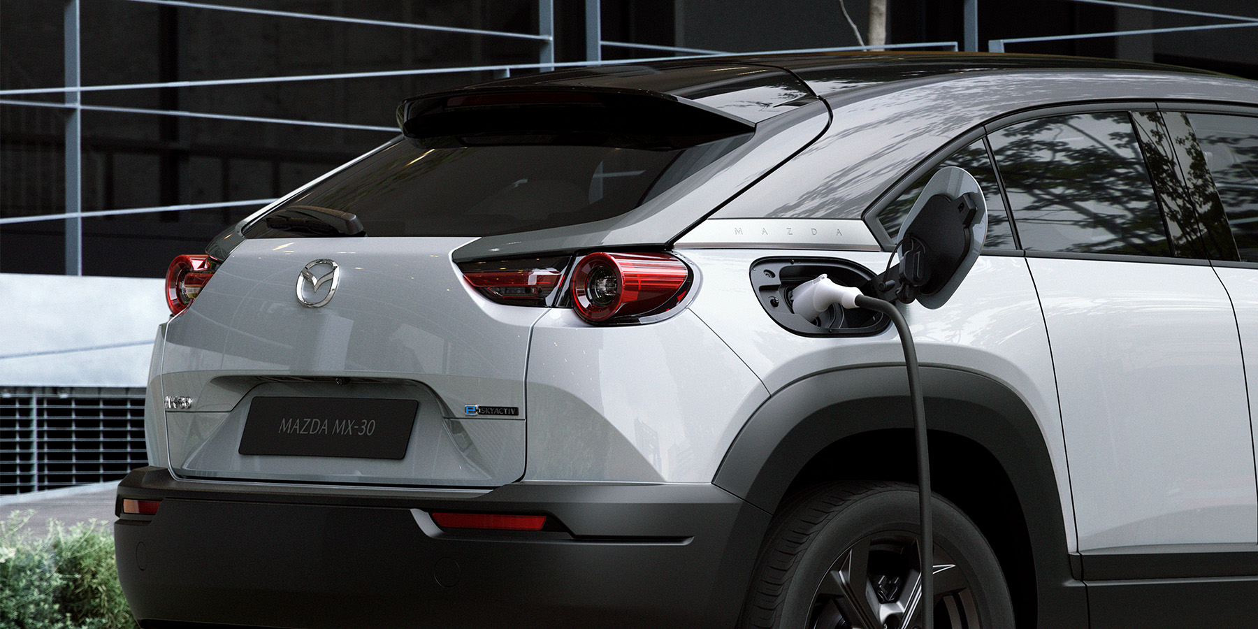Gros plan sur le port de recharge d'une Mazda MX-30 électrique, avec le câble branché et le voyant de charge allumé.