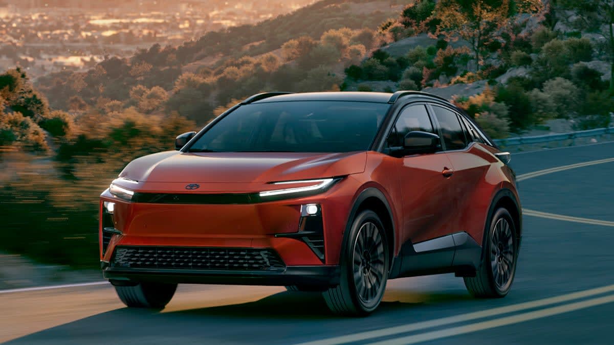 Un Toyota C-HR électrique 2026 de couleur vive, roulant sur une route sinueuse dans un paysage verdoyant.
