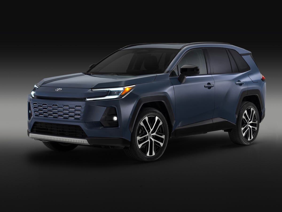 Un Toyota RAV4 Prime 2026 de couleur foncée, garé devant une borne de recharge dans un environnement urbain moderne.