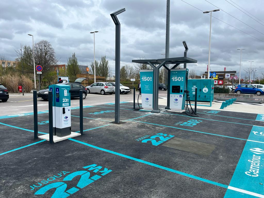 Une voiture électrique moderne en train de se recharger à une borne publique dans une ville française, avec des passants en arrière-plan.