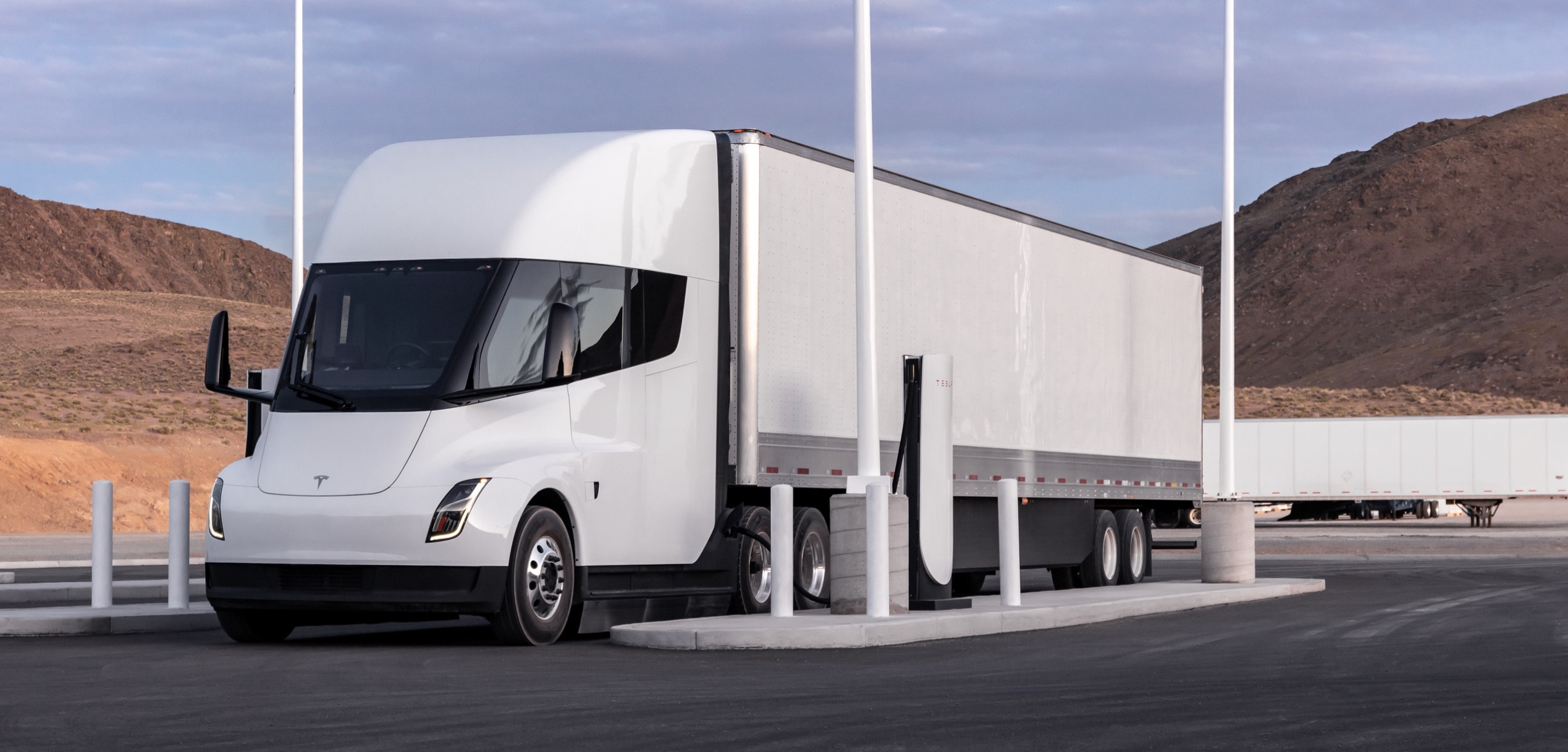 Un camion Tesla Semi blanc en train de charger à une station Megacharger, avec des bornes de recharge visibles.