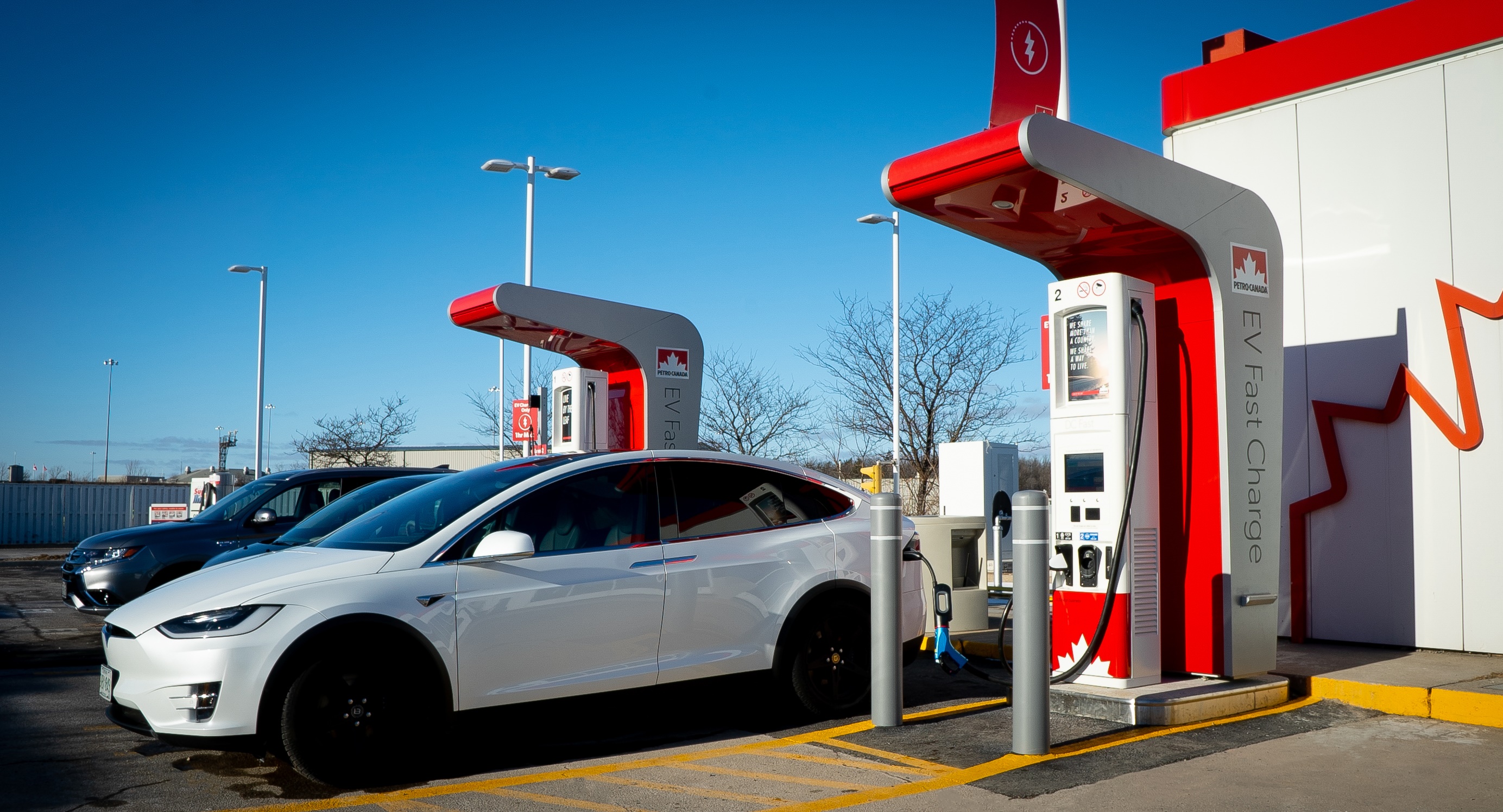 Plusieurs bornes de recharge publiques pour véhicules électriques alignées dans un environnement urbain canadien, avec des voitures en charge et des passants.