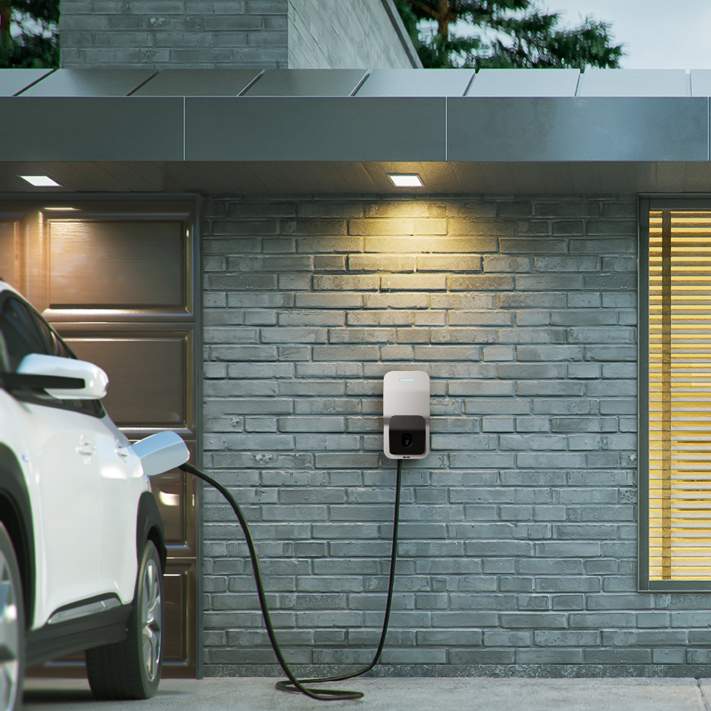 Une borne de recharge de véhicule électrique installée sur le mur d'une maison moderne au Canada, avec un véhicule électrique garé et en charge dans l'allée enneigée.