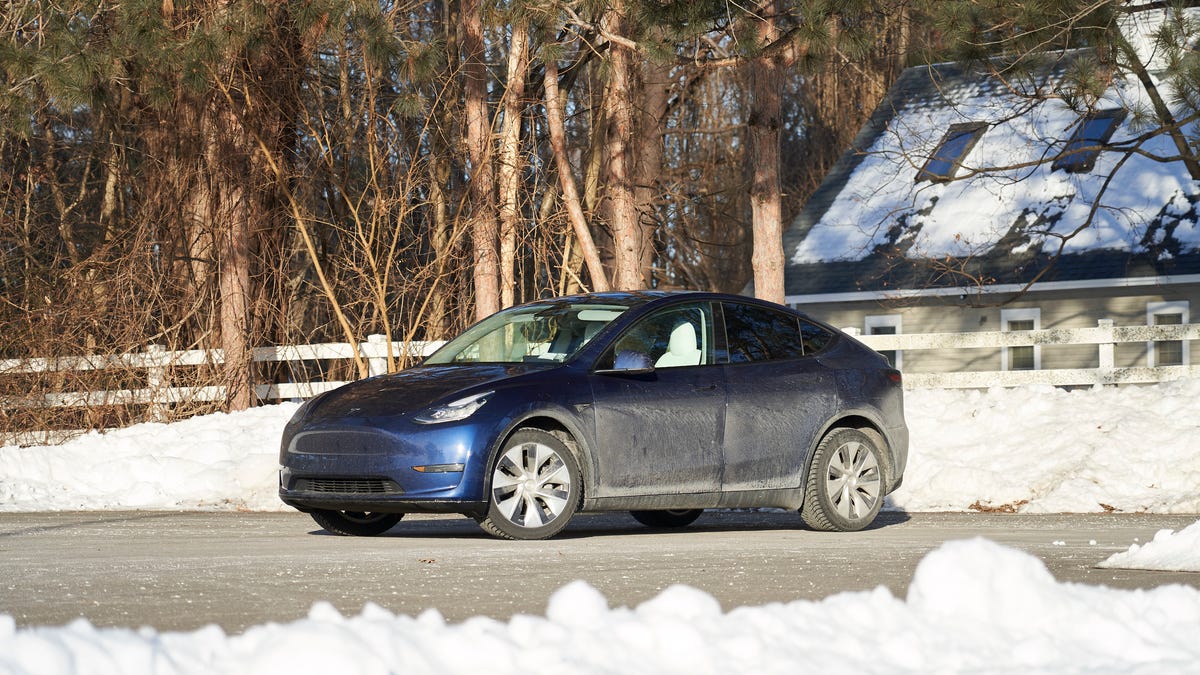 Une Tesla Model Y Long Range blanche roulant sur une route enneigée en hiver, avec des montagnes en arrière-plan.