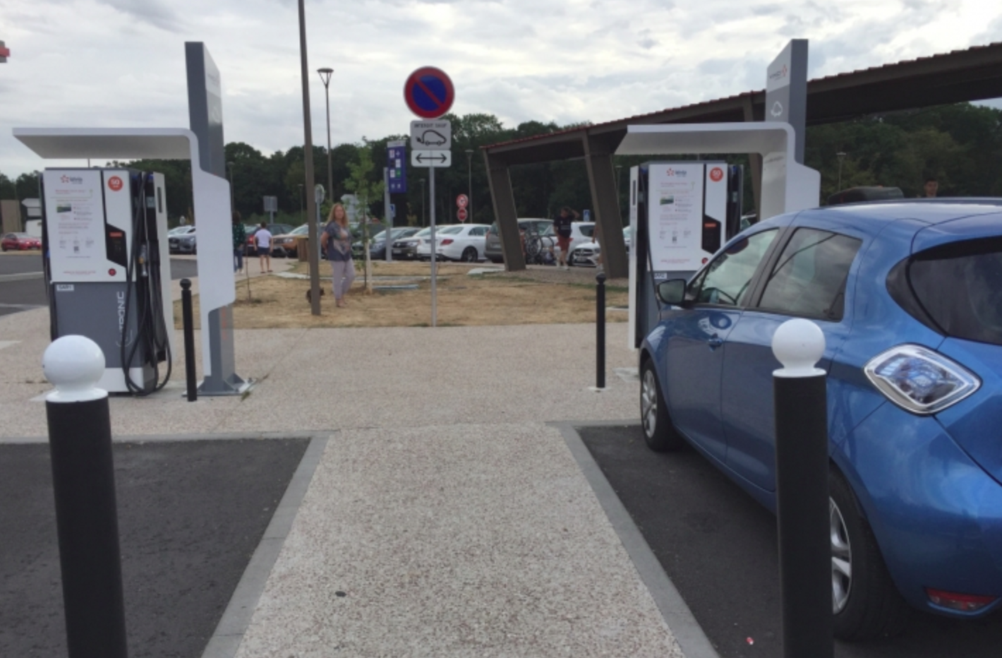 Personne utilisant une borne de recharge moderne pour voiture électrique en autopartage dans le Centre-Val de Loire, avec un paysage régional en arrière-plan.