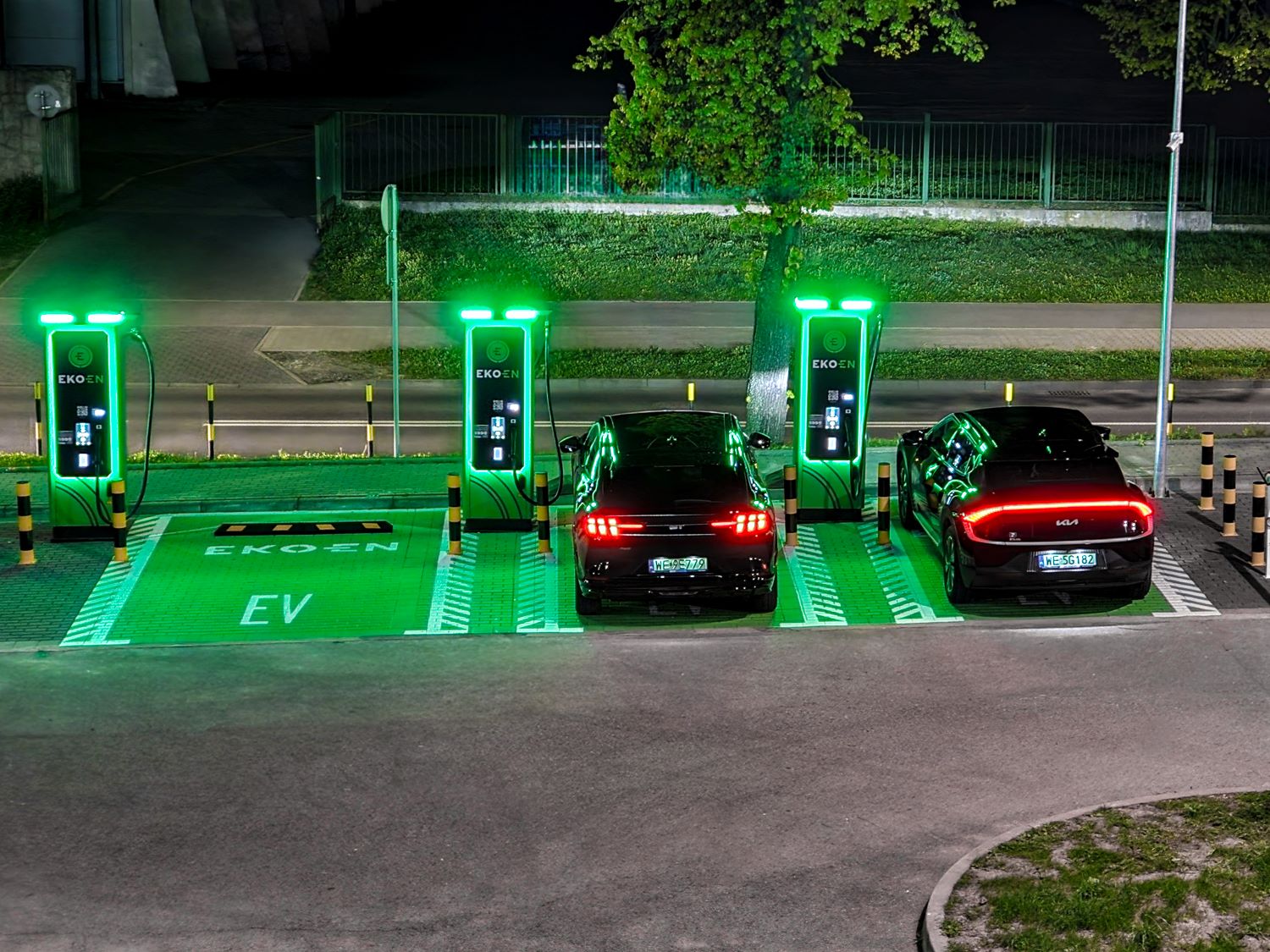 Plusieurs voitures électriques en charge sur une station d'autoroute animée en pleine journée, illustrant les coûts de recharge élevés en déplacement.