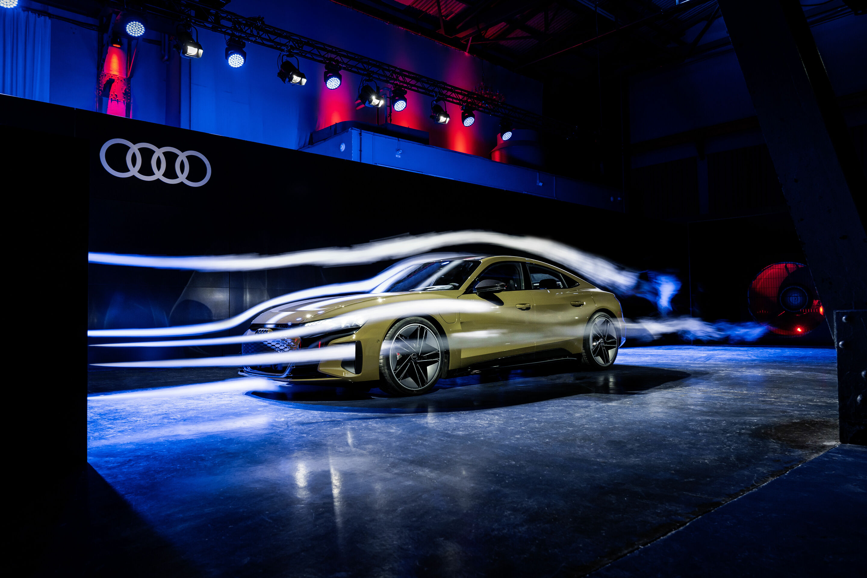 Une Audi e-tron GT de couleur vive en mouvement sur une route, vue sous un angle dynamique, mettant en valeur son design élégant.