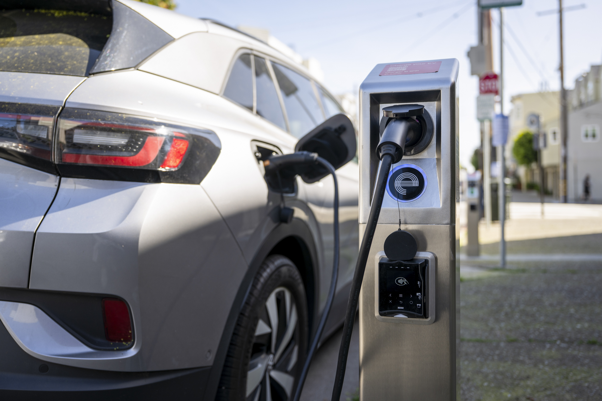 Une voiture électrique branchée à une borne de recharge au milieu de vignes en Bourgogne, avec un couple profitant d'un verre de vin au coucher du soleil.