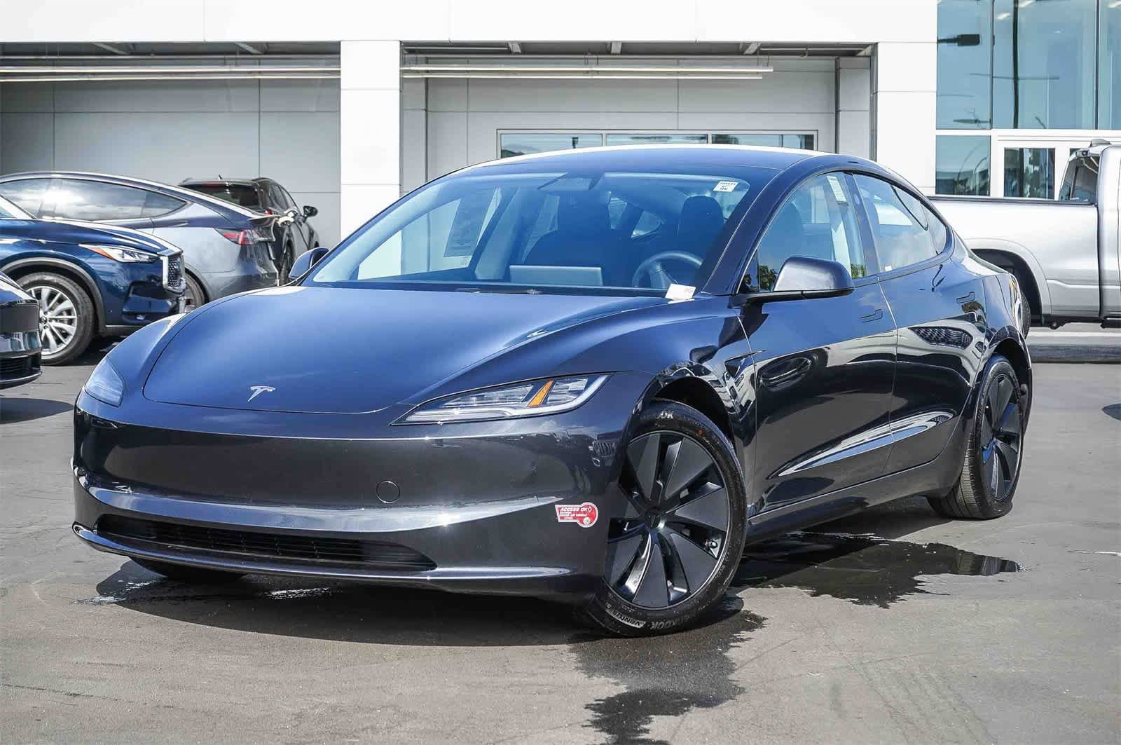 Une Tesla Model 3 Standard Plus RWD grise d'occasion, garée sur un parking de concessionnaire.