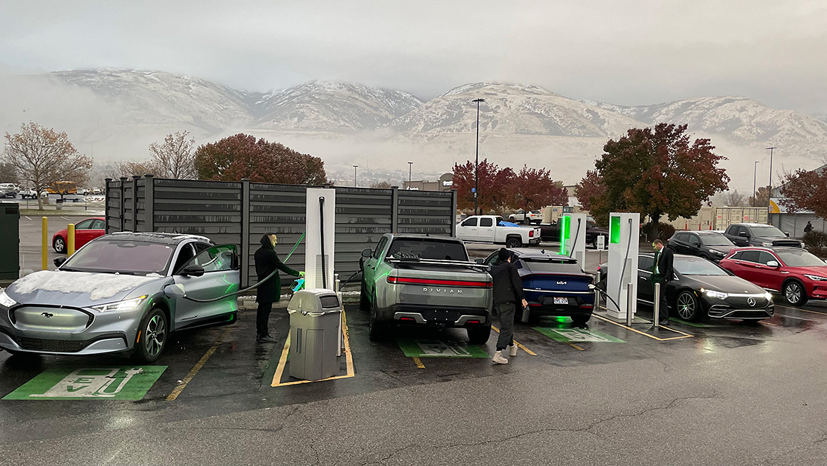 Une station de recharge de véhicules électriques bondée, avec plusieurs voitures en attente et toutes les bornes occupées, illustrant la saturation du réseau.