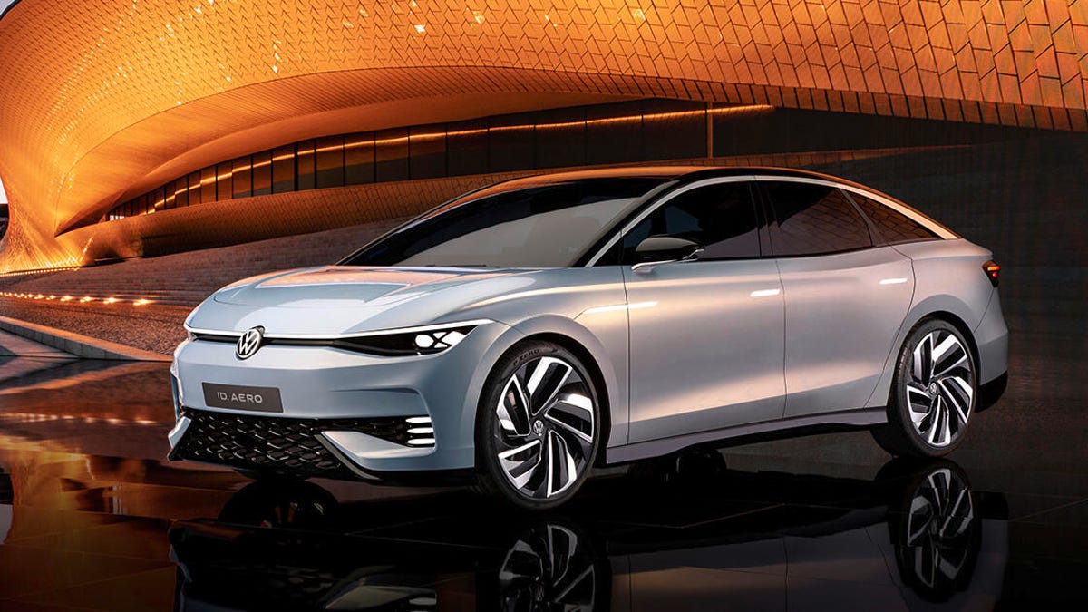 Vue latérale d'une berline électrique Volkswagen ID. Aero futuriste et élégante, de couleur argentée, exposée dans un showroom moderne.