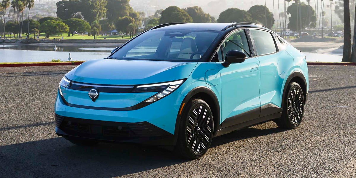 Une Nissan Leaf 2026 de couleur bleu nacré avec un toit noir, garée dans un environnement urbain moderne au crépuscule.