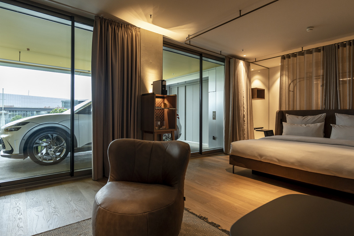 Une voiture électrique branchée à une borne de recharge devant un charmant hôtel en pierre, avec un couple se dirigeant vers l'entrée.
