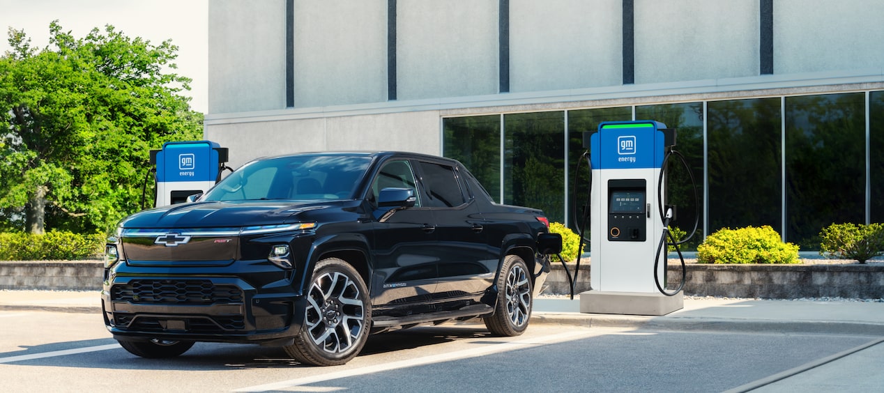 Un Chevrolet Silverado EV blanc branché à une borne de recharge rapide dans un environnement urbain.
