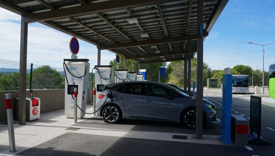 Une longue file de voitures électriques patientant pour recharger à une station très fréquentée sur une autoroute française en plein été.