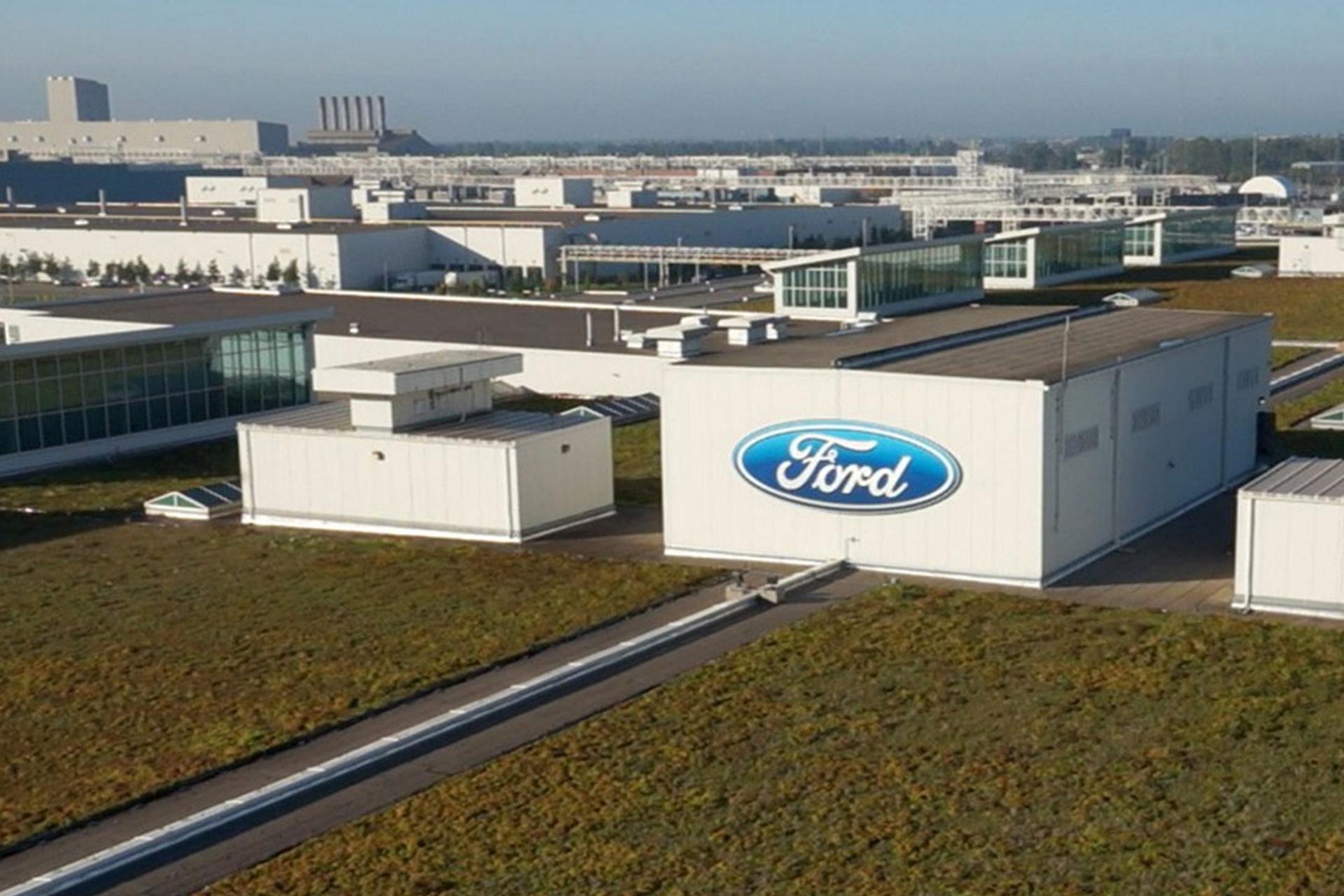 Une vue aérienne montre l'immense complexe industriel de Ford BlueOval City, avec plusieurs bâtiments modernes et des zones de production distinctes, entourés de verdure.