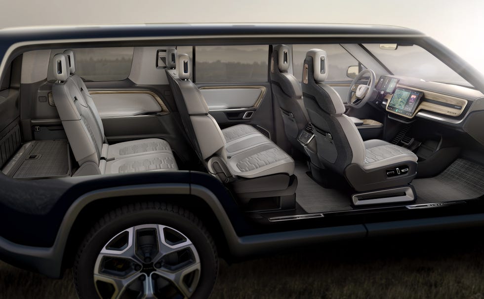 L'intérieur d'un SUV électrique Rivian R1S, montrant le tableau de bord numérique, le grand écran central et les sièges en cuir clair.