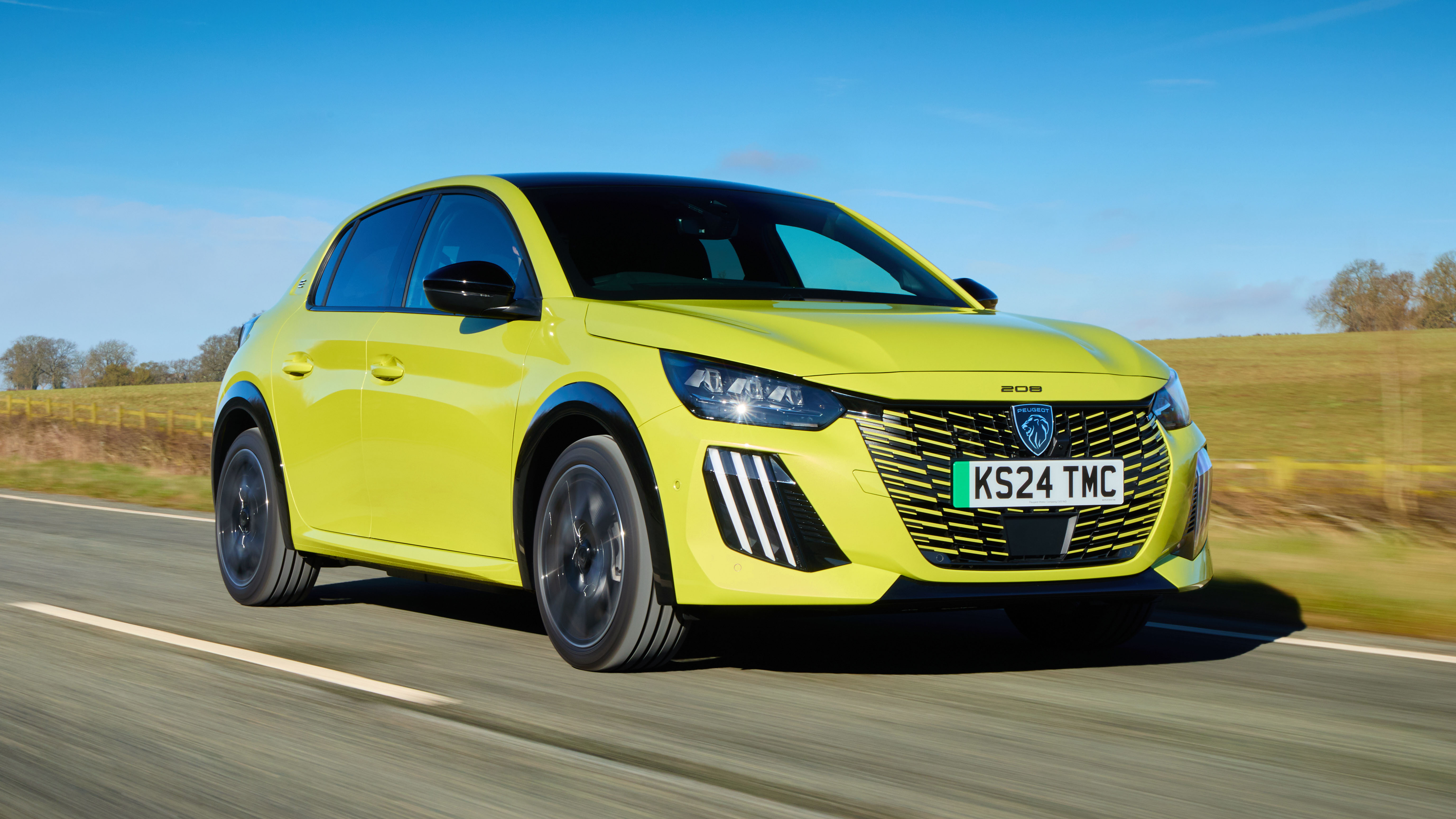 Une Peugeot e-208 bleue de 2026 en charge à une borne publique, avec des bâtiments urbains en arrière-plan.