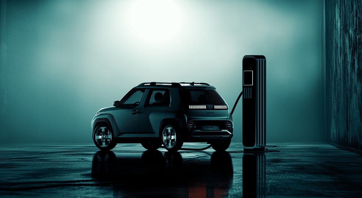 Une Hyundai Inster blanche branchée à une borne de recharge rapide dans une rue de ville animée, avec des bâtiments modernes en arrière-plan.