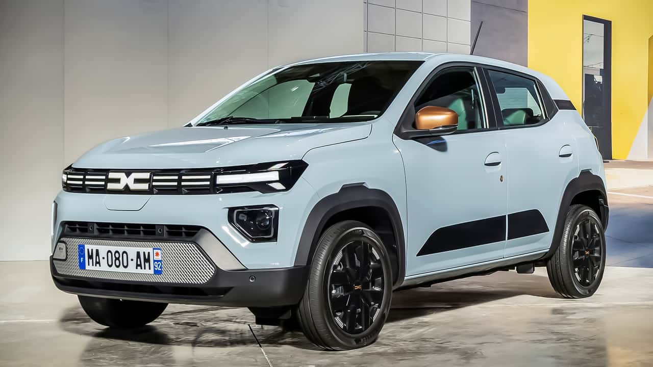 Une Dacia Spring 2026 blanche en train de charger sur une borne électrique en Norvège, avec des montagnes et un fjord en arrière-plan.