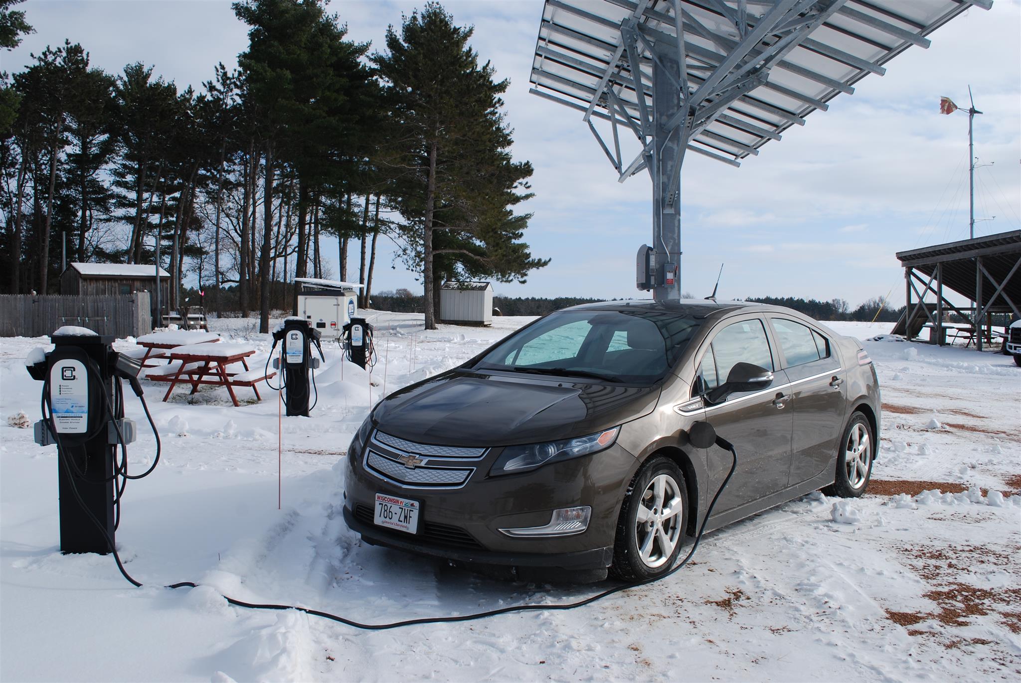 Une voiture électrique blanche branchée à une borne de recharge sous une légère chute de neige, illustrant le préchauffage en hiver.