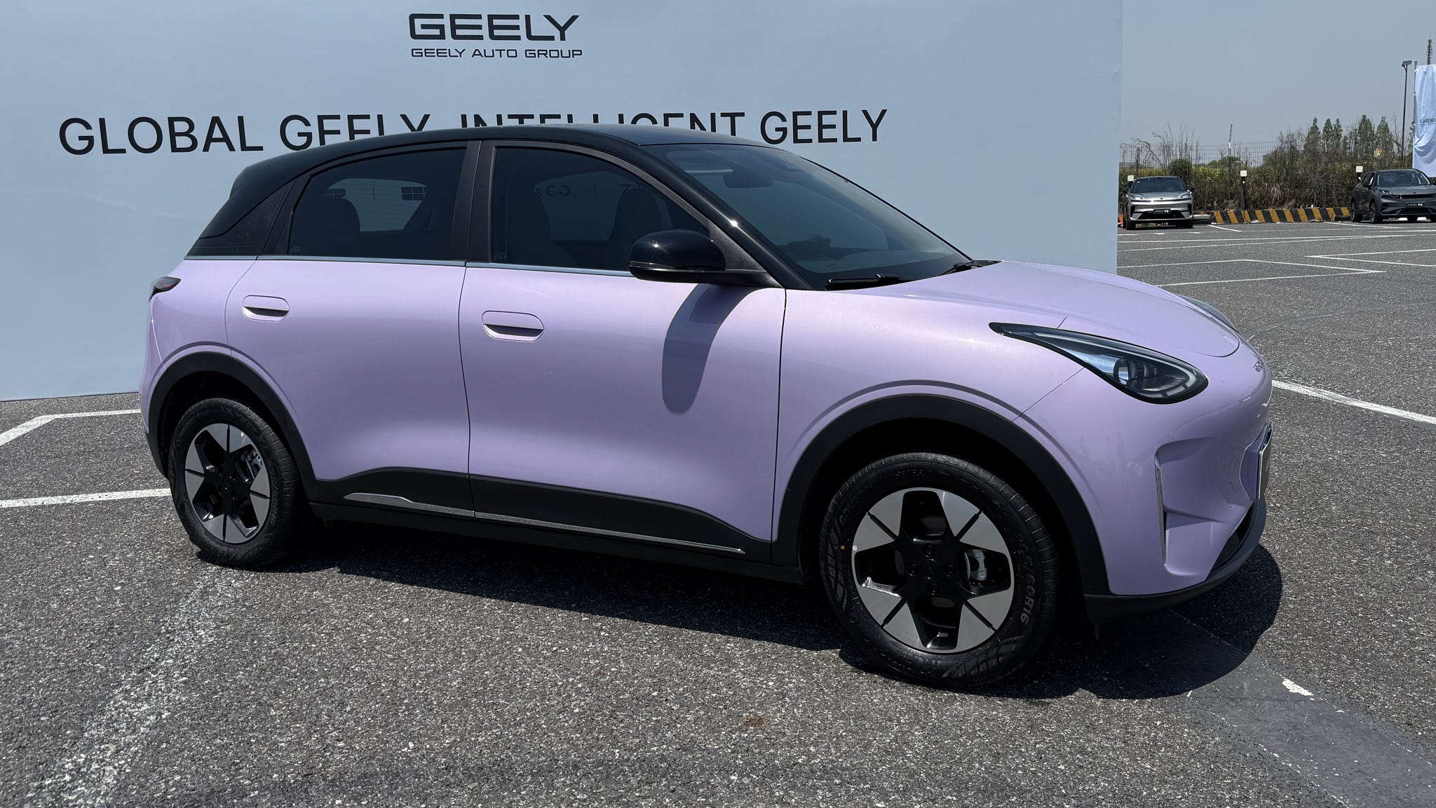 Vue latérale d'une berline électrique Geely EX2 de couleur vive, sur une route futuriste.
